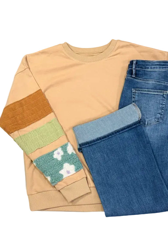 Beige sweatshirt with green accents and blue jeans on a white background